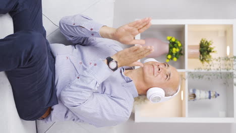 Vertical-video-of-Happy-old-man-at-home-calmly-listening-to-music-on-headphones.
